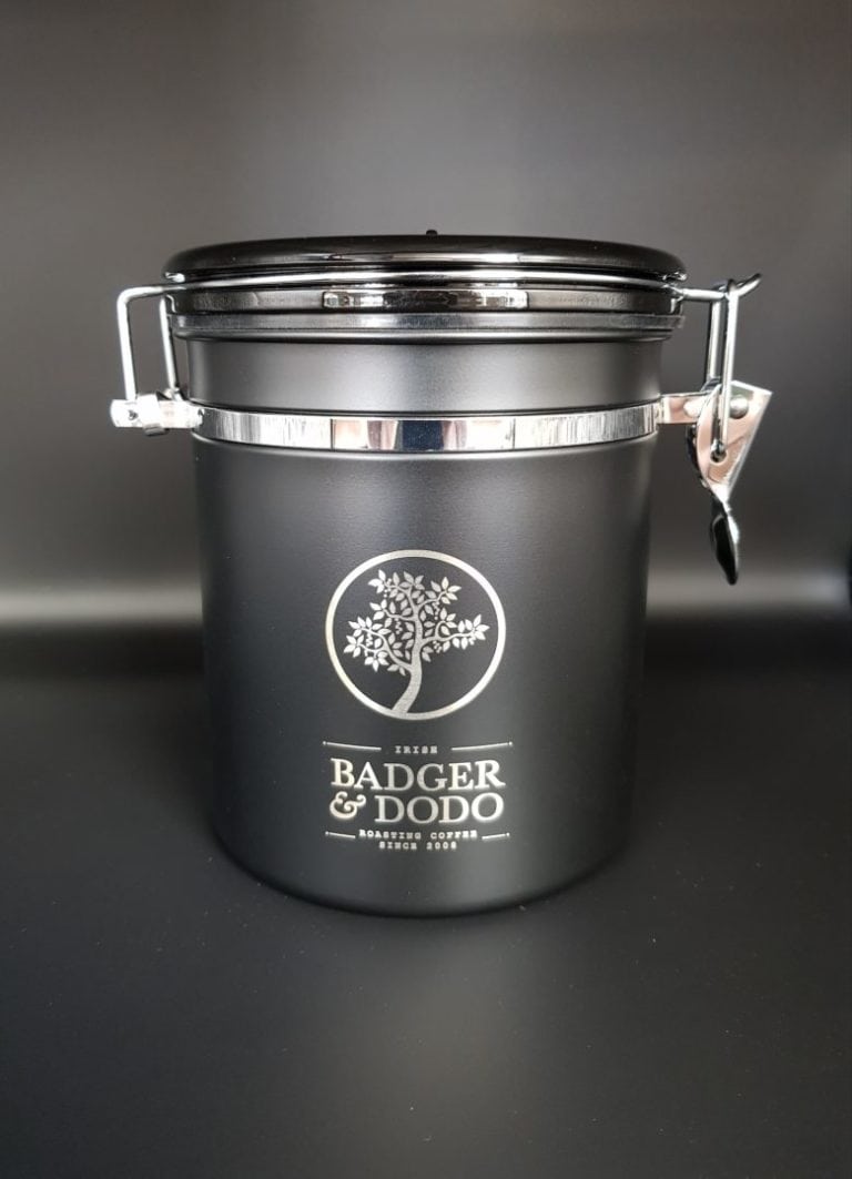 Badger and Dodo Coffee Roasters: A black metal coffee canister with a silver latch and airtight seal, featuring Badger & Dodo roastery branding and a tree logo, set against a plain dark background.