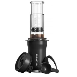 Black AeroPress coffee maker with a clear brewing chamber and plunger assembled on top of an insulated travel tumbler. A black lid and measuring scoop are placed beside the tumbler, all displayed against a white background.