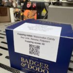 Close-up of navy blue Badger & Dodo coffee box with gold logo, and a white label reading 'Colombia, Jario Arcila, Co Fermented Watermelon, Region: Armenia, Quindio, Farm: Santa Monica, Varieties: Castillo