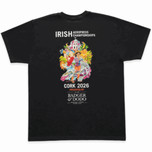 Back of a black T-shirt featuring colorful artwork of people, a church, tropical flowers, a dragon, and a coffee cup, with white text reading “Irish Aeropress Championships,” “Cork 2026,” and “Presented by Badger & Dodo Roasting Coffee.