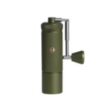 A green manual coffee grinder with a cylindrical textured body, a crank handle on the side, and a small circular logo on the front, shown against a white background.